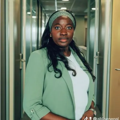 Femme portant un blazer vert et un bandeau, debout dans un couloir lumineux.