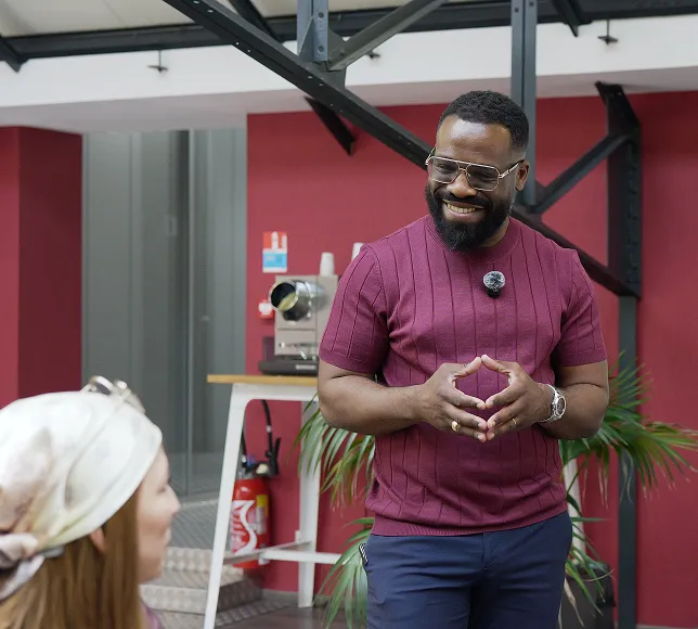 Homme souriant en pull bordeaux discutant avec une femme portant un foulard en intérieur.