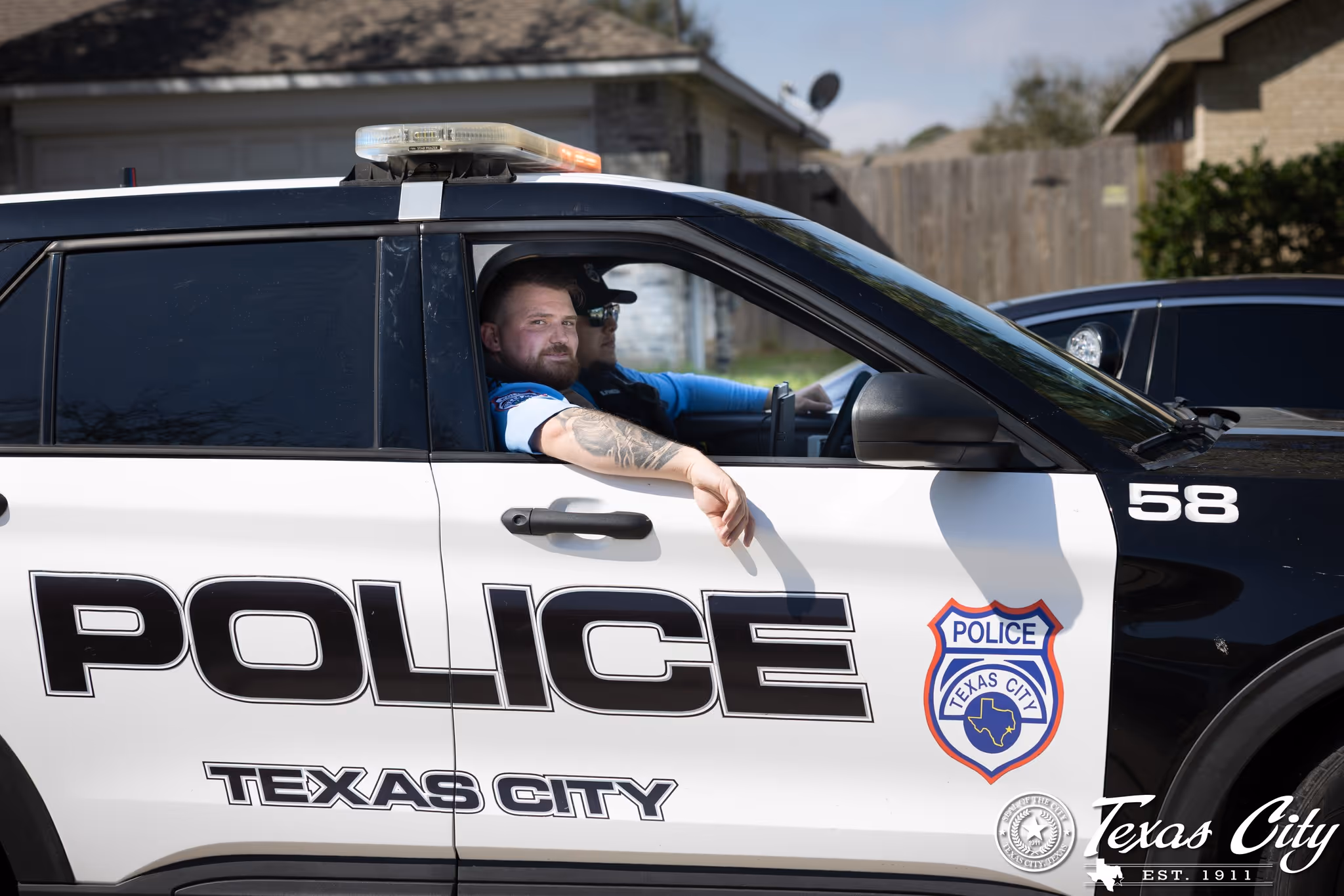 Two Texas City police officers in a black-and-white patrol car with door number 58 and badge emblem.