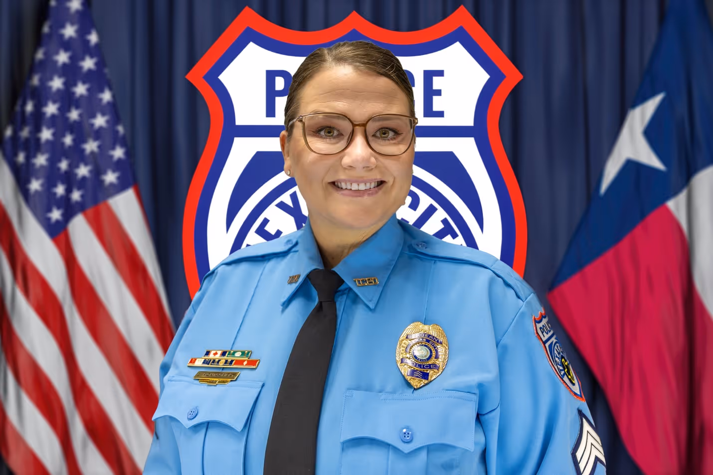 Smiling female police officer in uniform with badges, in front of American and Texas flags and police shield.