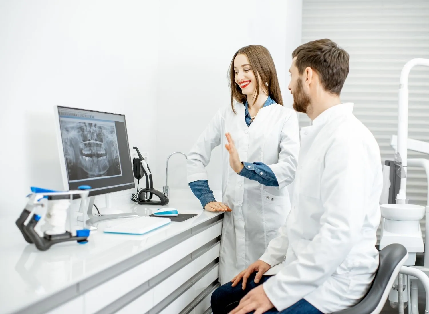 Female dentist explaining dental X-ray to male colleague in a dental clinic.