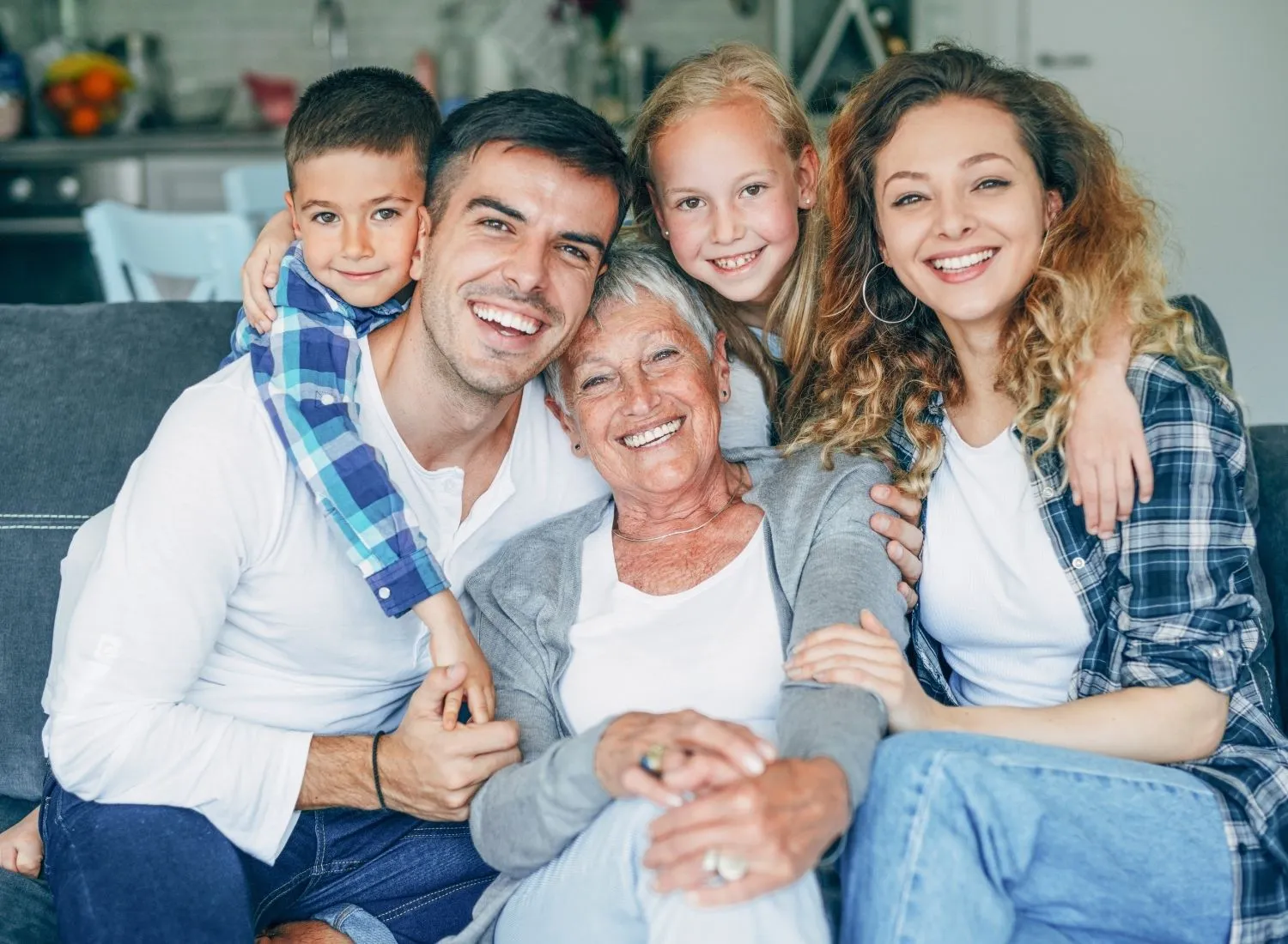 Smiling multi-generation family sitting close together on a couch in a cozy home setting.