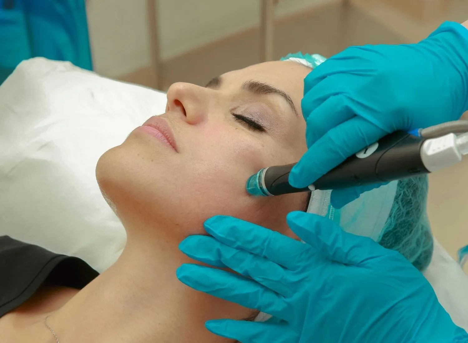Close-up of a woman receiving a facial treatment with a handheld device by a gloved technician.