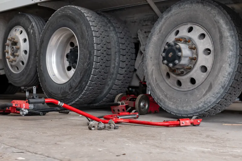 Heavy-duty tire service on semi axles with red jacks, loose lug nuts, and visible Goodyear sidewalls.