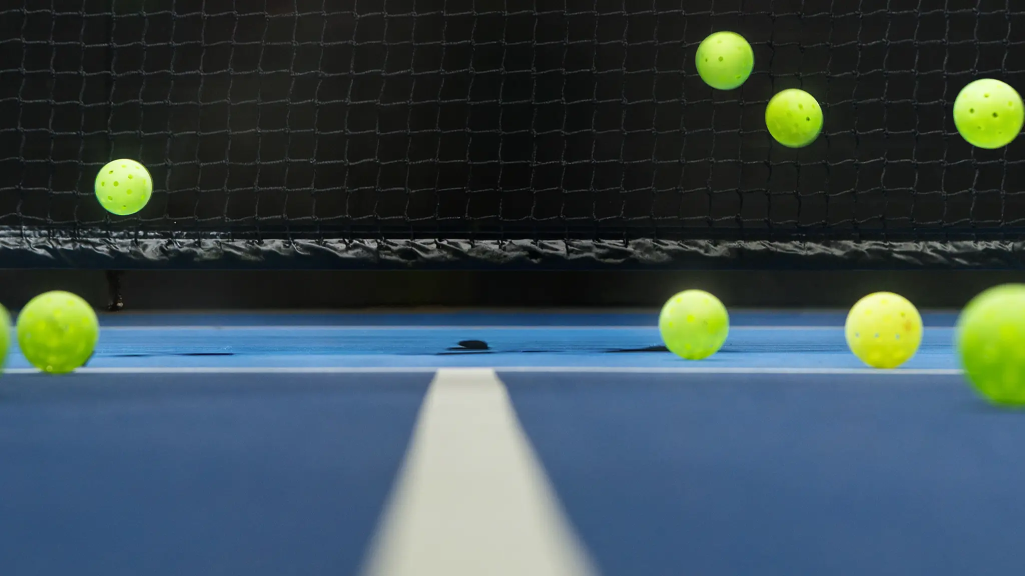 Multiple yellow-green pickleball balls bouncing near a net on a blue court surface, at a Keystone Pickleball tournament.