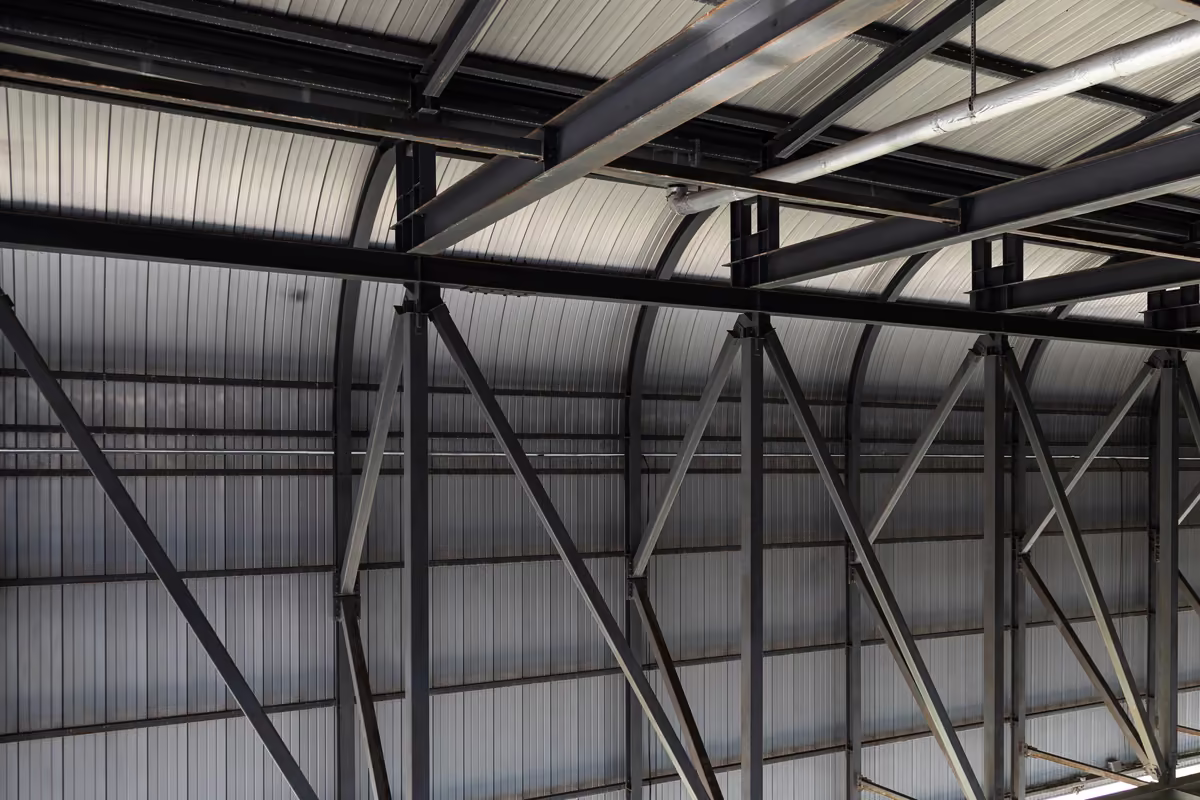Interior view of industrial building ceiling with steel beams and metal panel roofing.