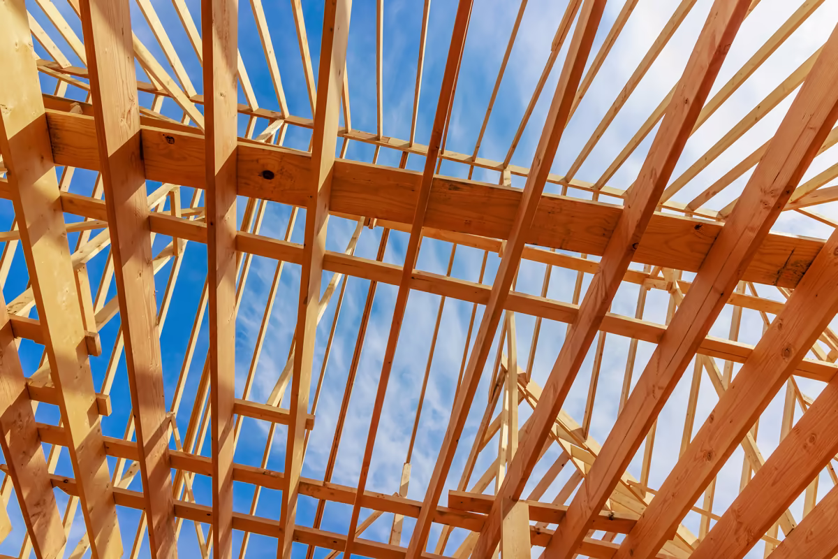 Wooden framing structure of a building under construction against a blue sky with some clouds.