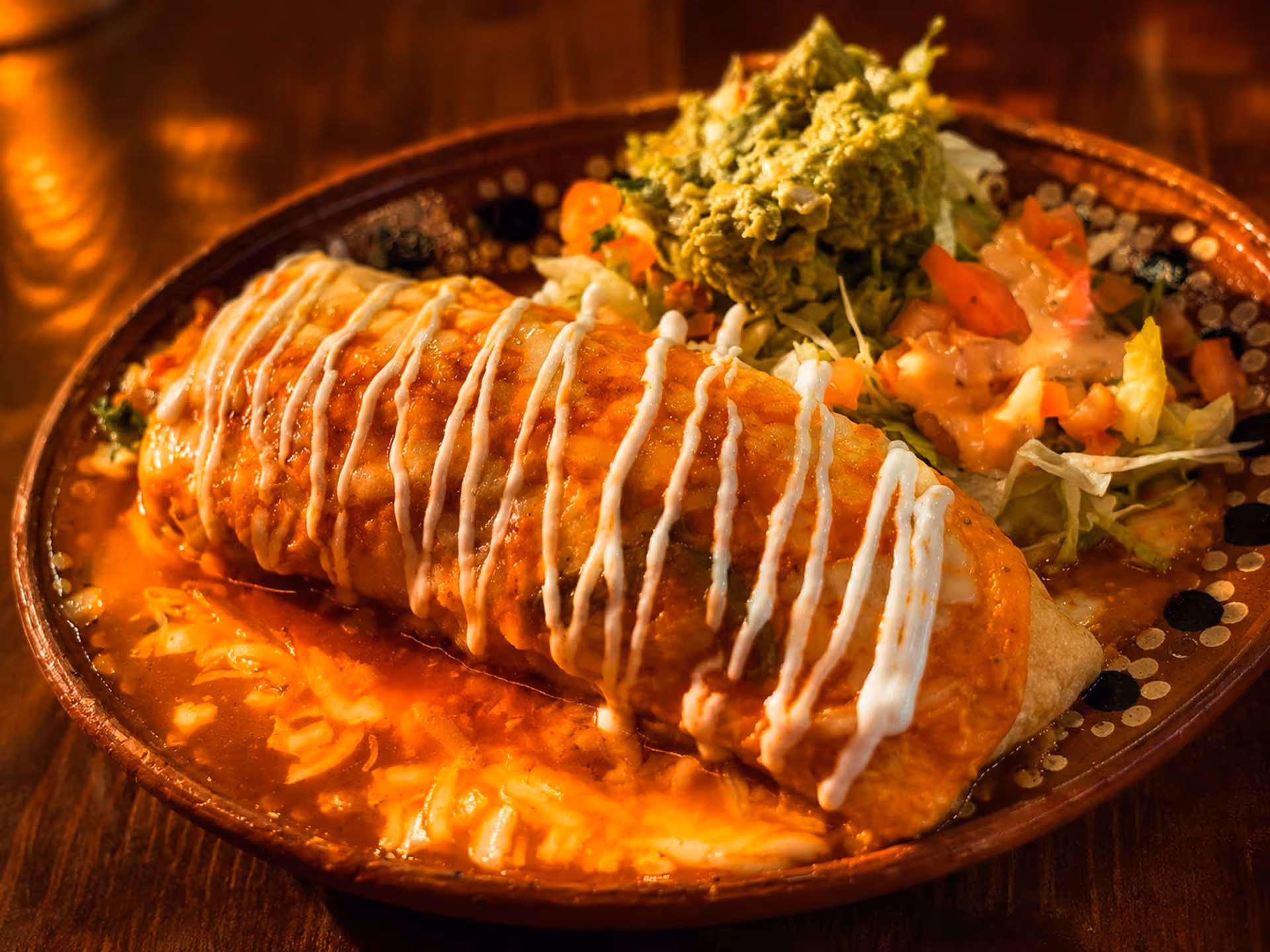 A plate of food with a burrito, salad, and sour cream.