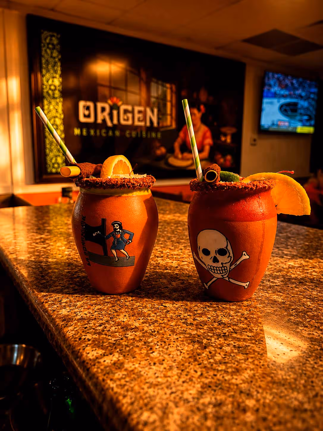Two drinks with straws and skulls on them sit on a counter.