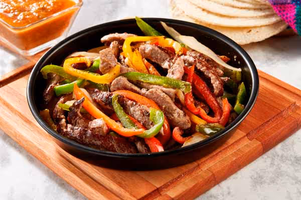 A bowl of Mexican beef fajitas served with warm tortillas and a side of salsa.