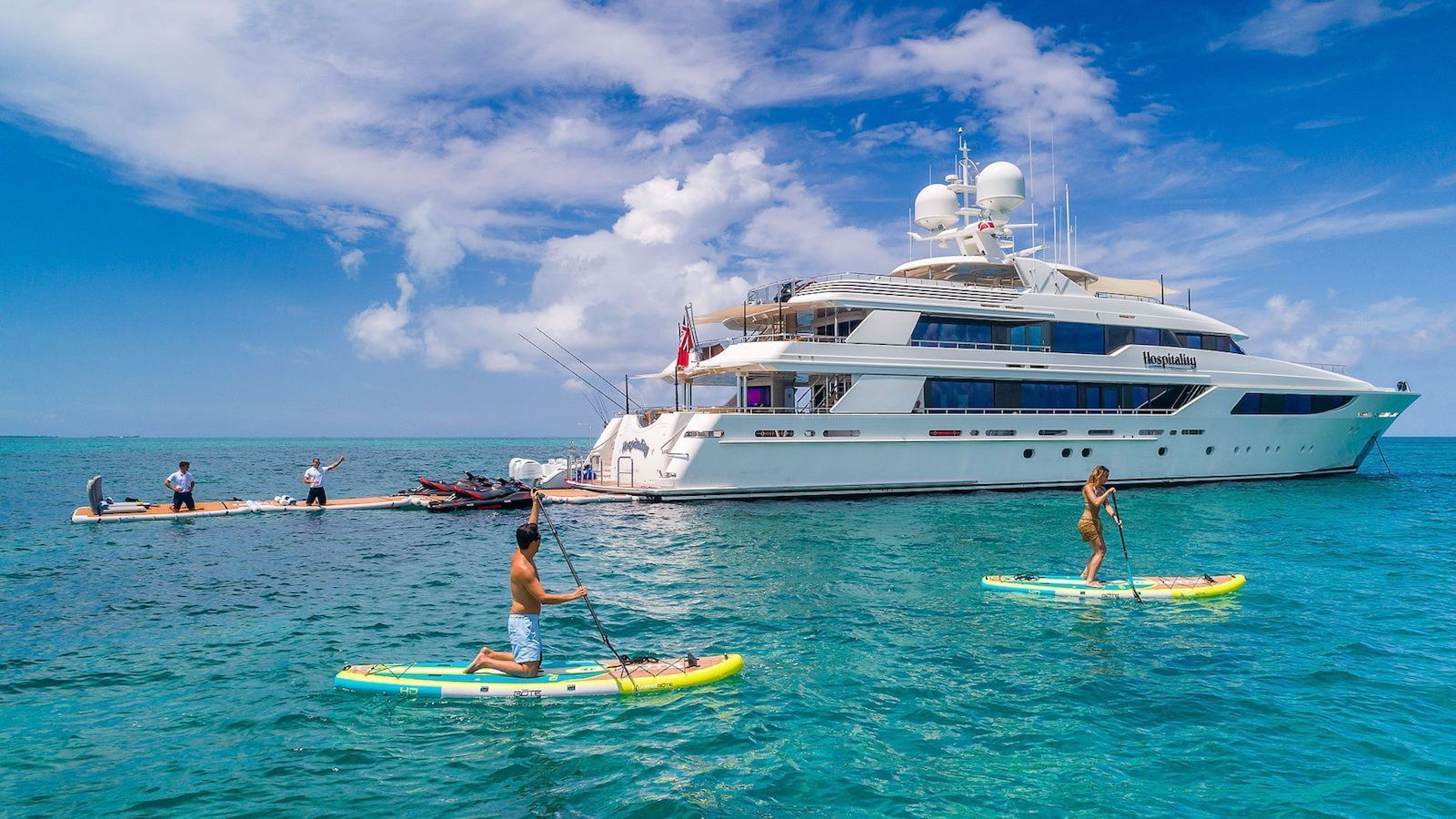 Guests paddleboarding beside a motor yacht at anchor