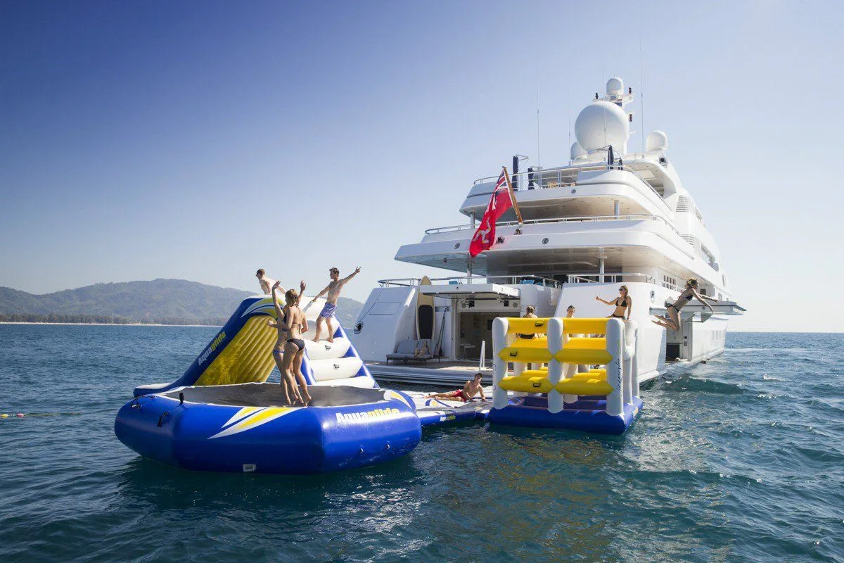 Guests on an inflatable slide and climbing tower beside a superyacht
