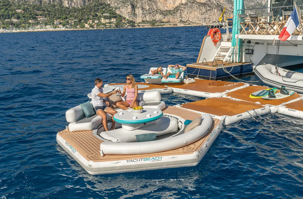 Guests at a YACHTBEACH Hex pavilion lounge linked to platforms behind a catamaran