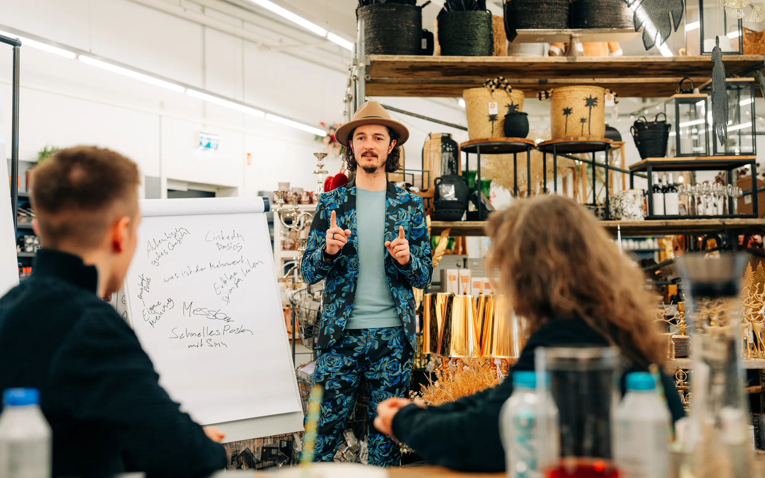 Mann im Blumenanzug hält Workshop vor Flipchart in einem Geschäft mit Dekorationsartikeln.