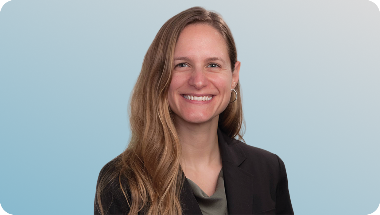 Smiling woman with long light brown hair, wearing hoop earrings and a black blazer on blue background.