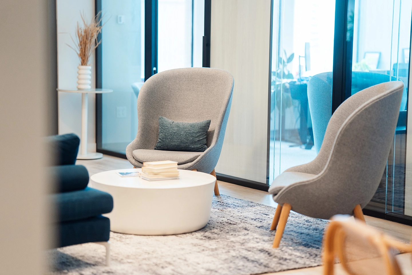 Modern office lounge with gray armchairs, a white round table, and a blue cushion.