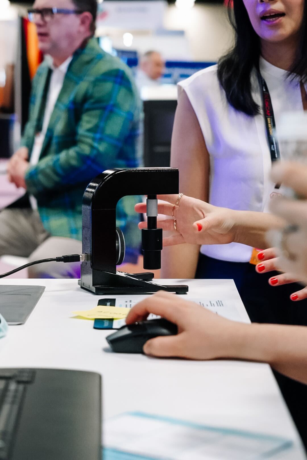 Person adjusting a black device on a table with another hand using a computer mouse nearby.
