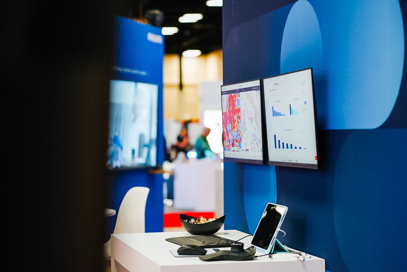 Workspace with dual monitors showing charts, a keyboard, mouse, tablet, and bowl on a white desk.