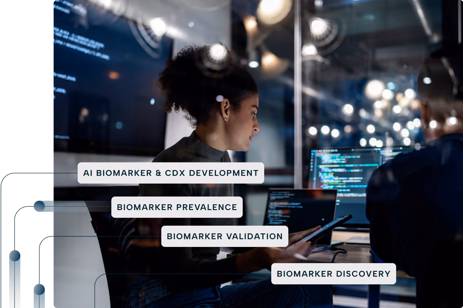 A young woman with curly hair is sitting in a modern office, working on a tablet and a laptop displaying code, with digital text overlays reading AI biomarker & CDx development, biomarker prevalence, biomarker validation, and biomarker discovery.