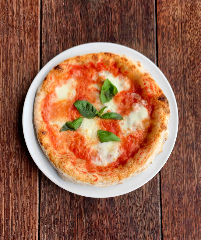 Margherita pizza with tomato sauce, melted cheese, and basil leaves on a white plate on wood table.