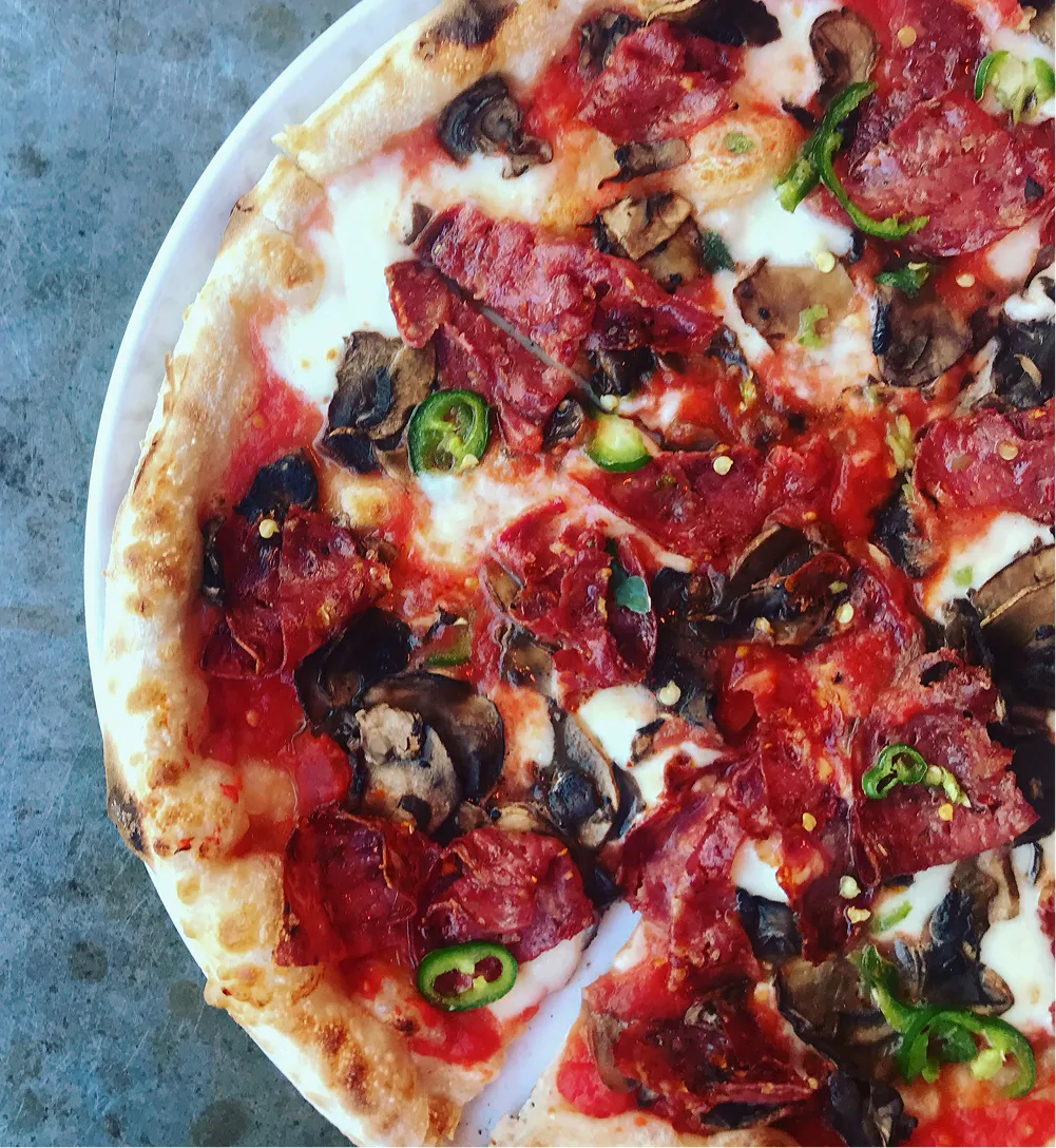 Pizza with pepperoni, mushrooms, jalapeño slices, and melted cheese on a white plate.