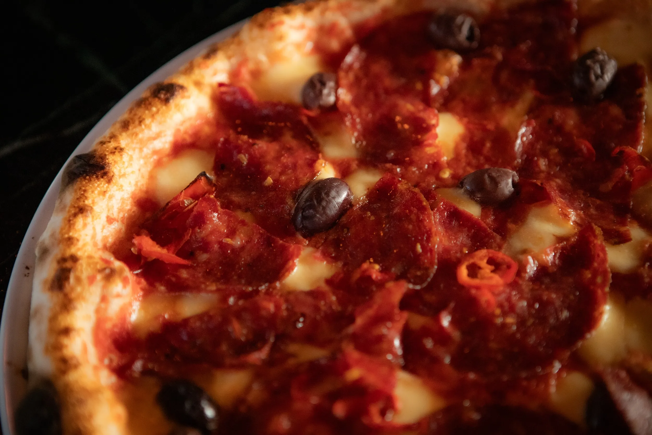 Close-up of pizza with pepperoni, black olives, melted cheese, and a golden crust on a white plate.