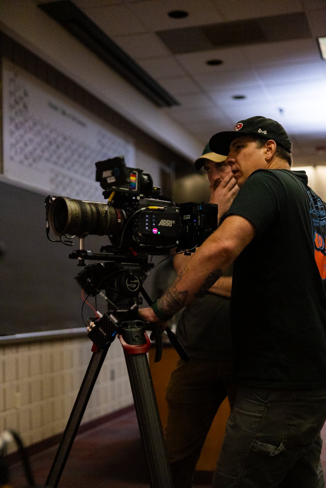 Camera on a tripod in a lecture hall, crew framing the shot