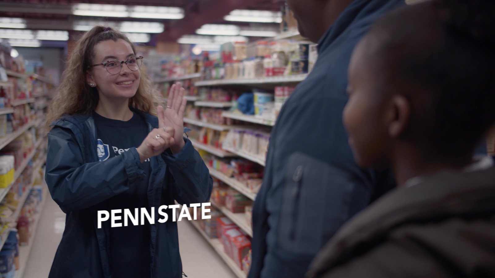 Student in a Penn State jacket high-fiving a shopper in a grocery aisle
