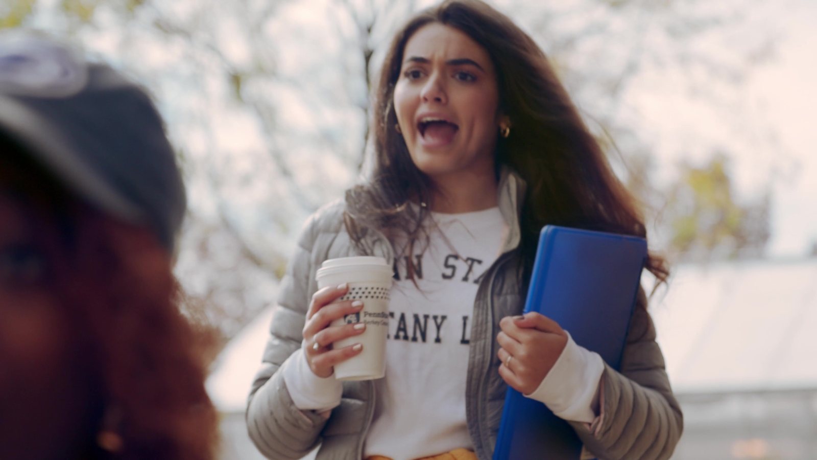 Student calling out We Are on campus with a coffee in hand