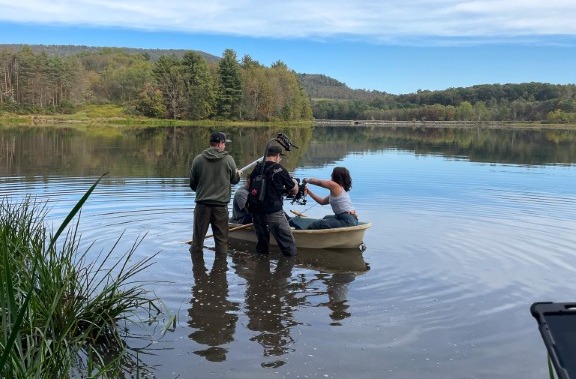 DMK crew wading into a lake to film a scene in a small boat