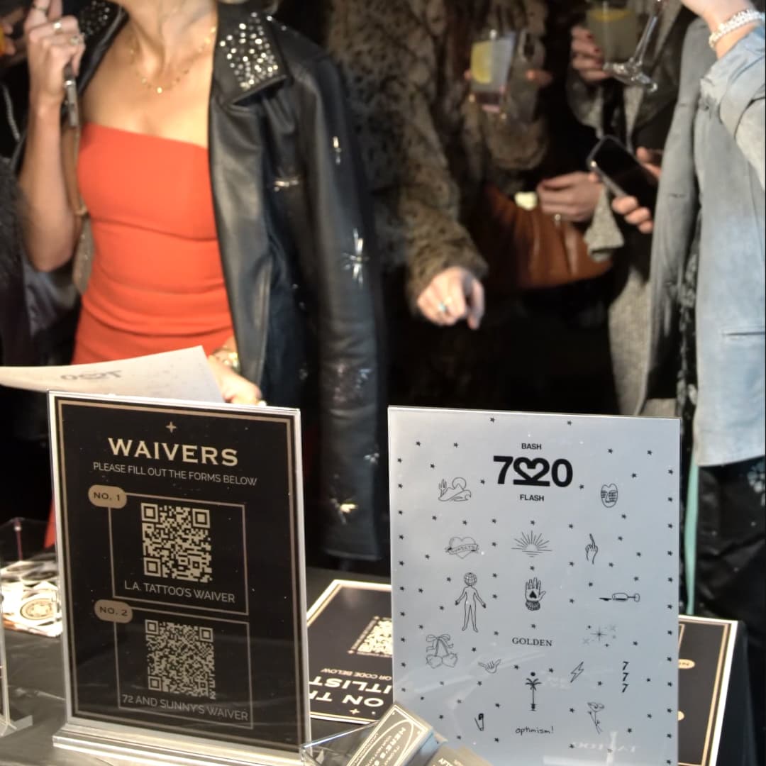 People at a counter with waiver QR codes and tattoo flash art displays visible.