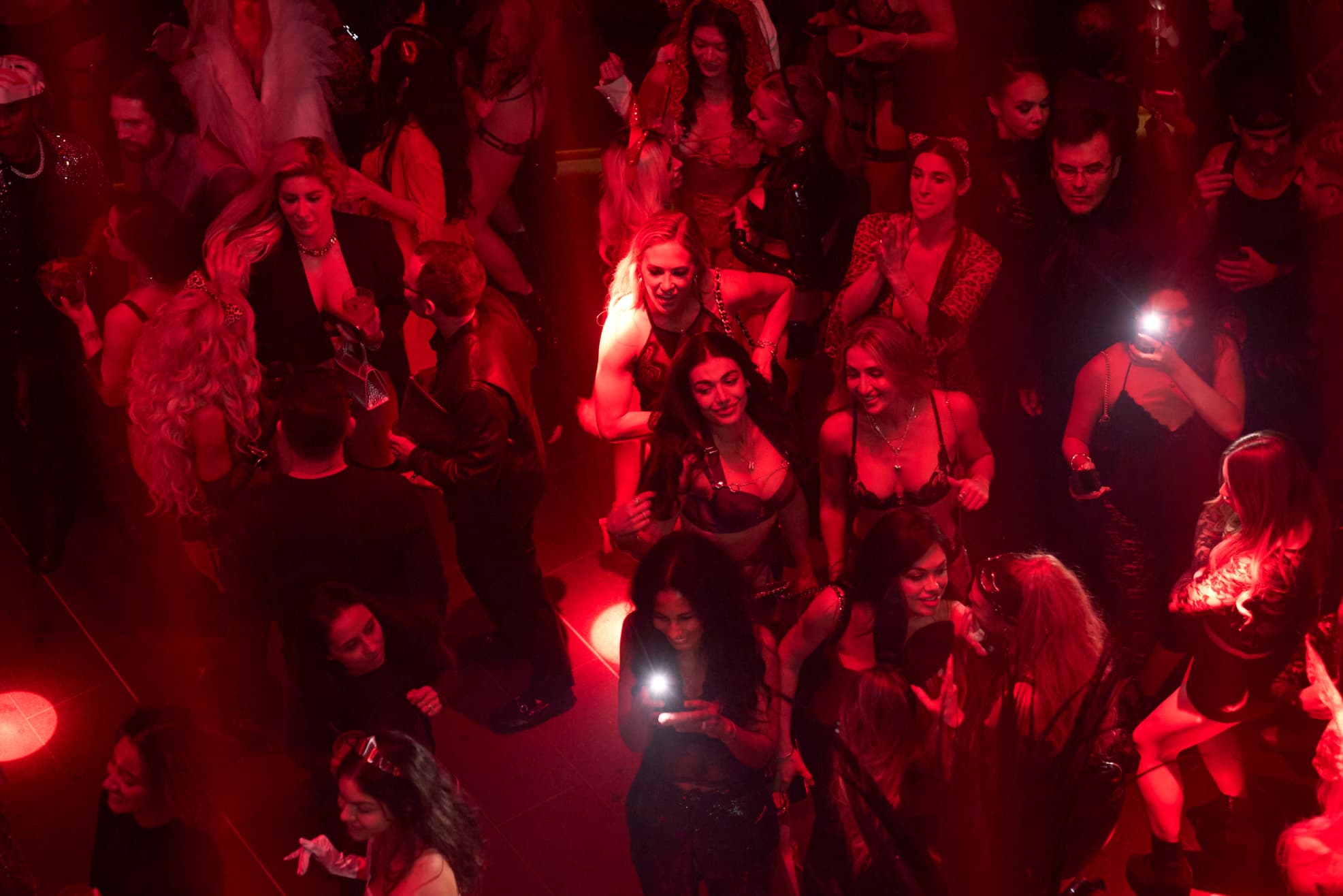 Overhead view of people dancing and socializing in a red-lit nightclub setting.