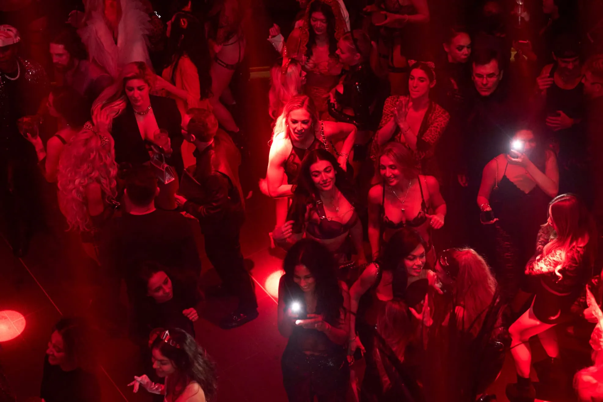 Overhead view of people dancing and socializing in a red-lit nightclub setting.