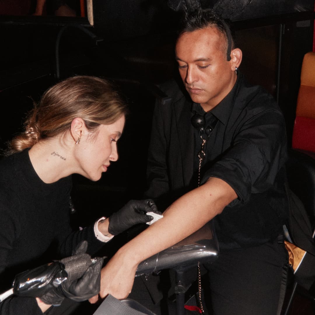 A tattoo artist wearing black gloves cleaning a man's arm before tattooing in a dimly lit setting.