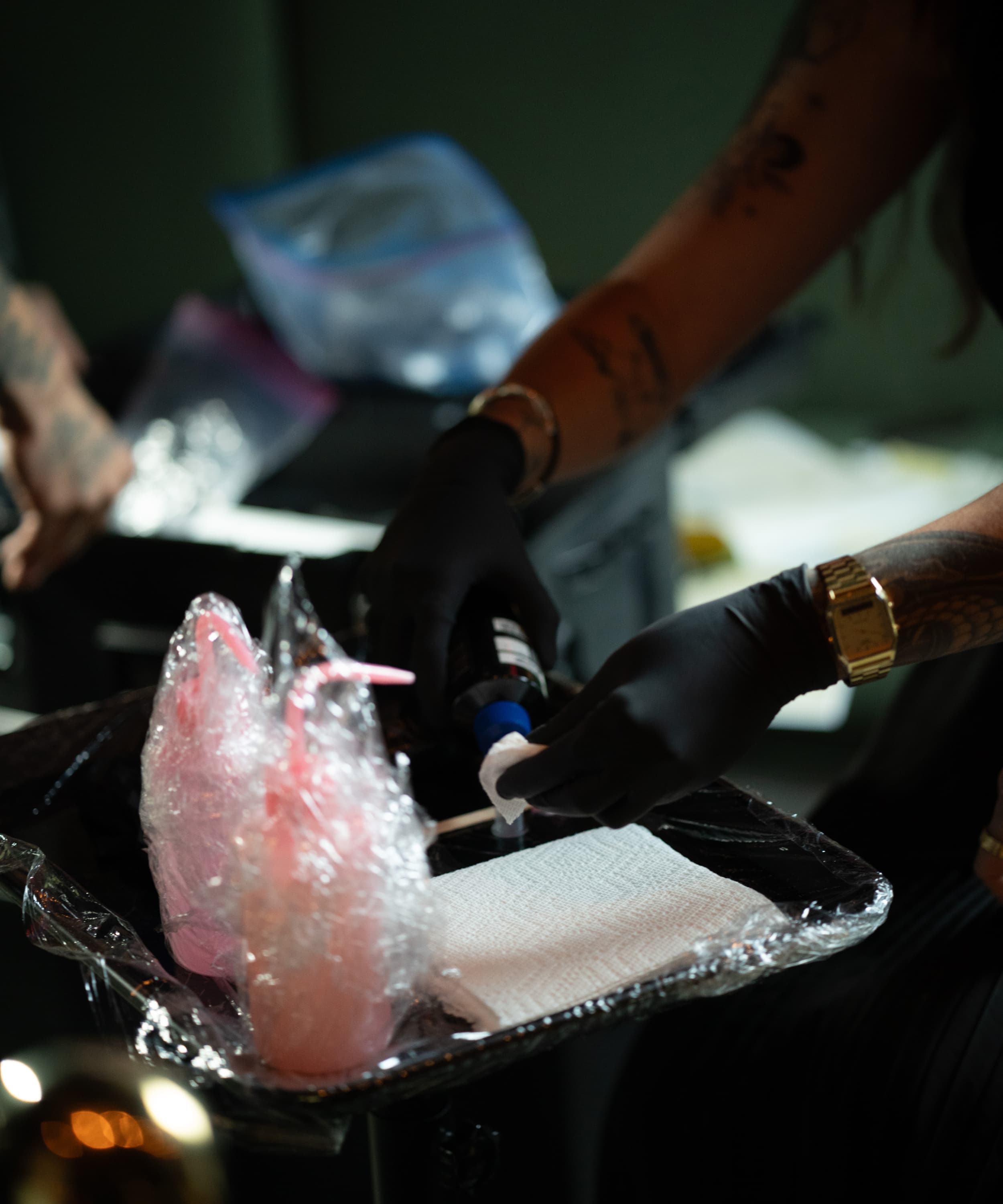 Tattoo artist wearing gloves preparing ink on a tray covered with plastic wrap and a paper towel.