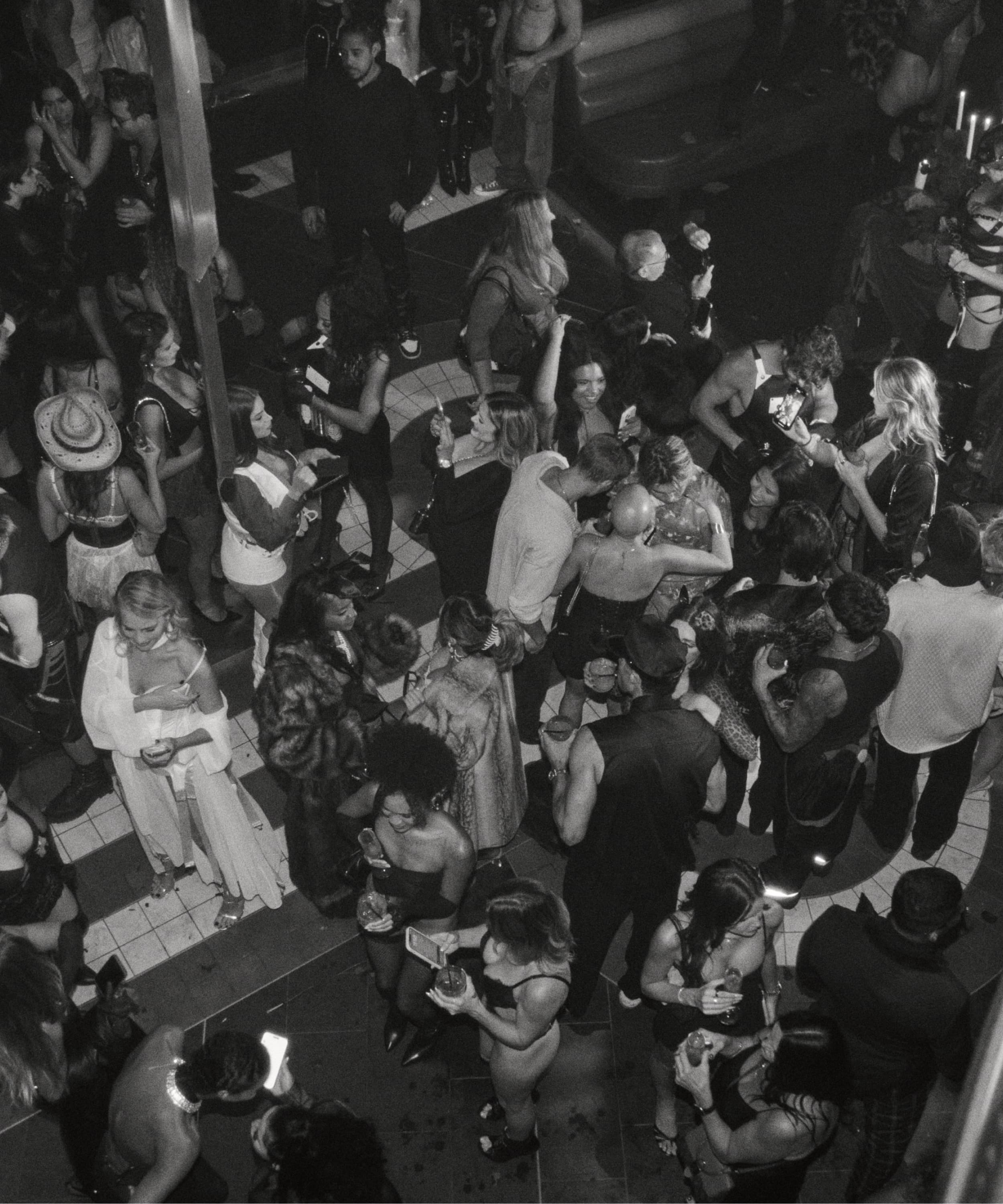 Overhead black and white photo of a crowded party with people chatting and holding drinks.