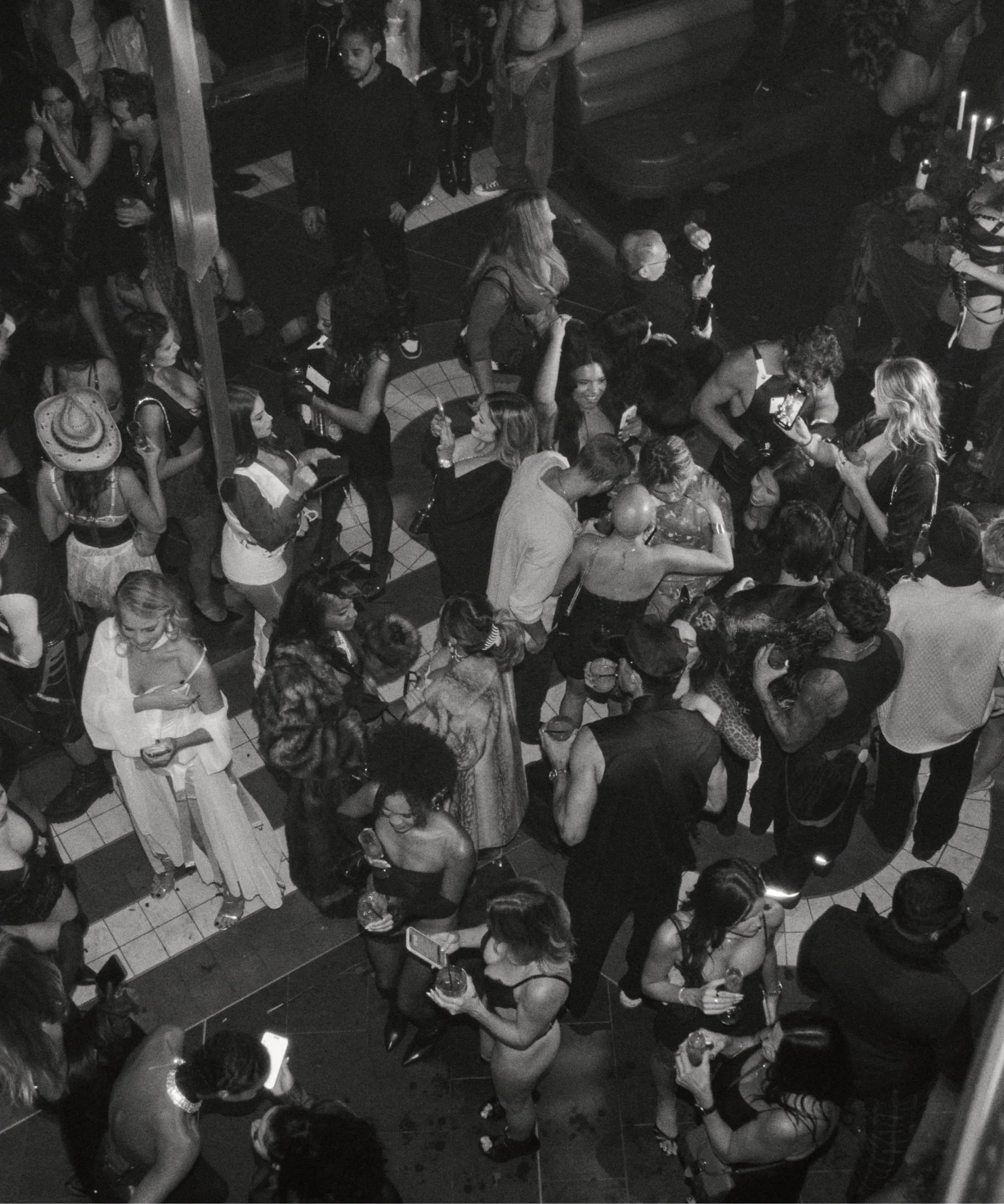 Overhead black and white photo of a crowded party with people chatting and holding drinks.