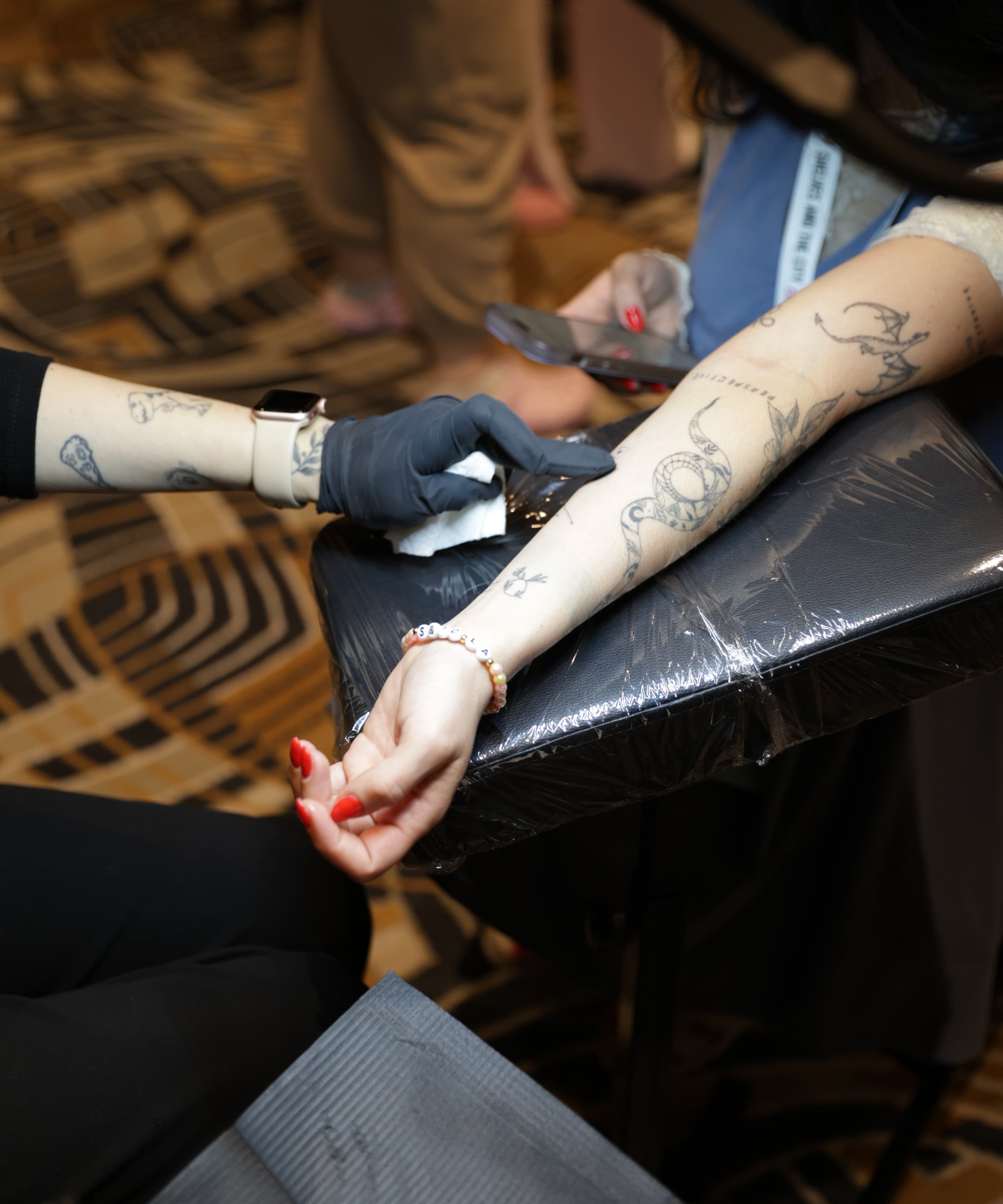 Person wearing black gloves cleaning a tattoo on an arm with a snake tattoo and bracelet.