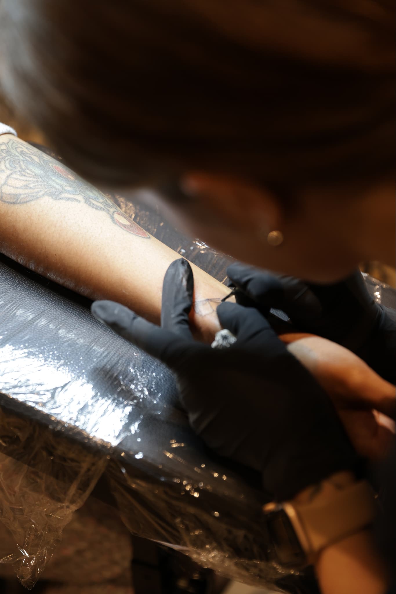 Tattoo artist wearing black gloves working on a tattoo on a client's forearm.
