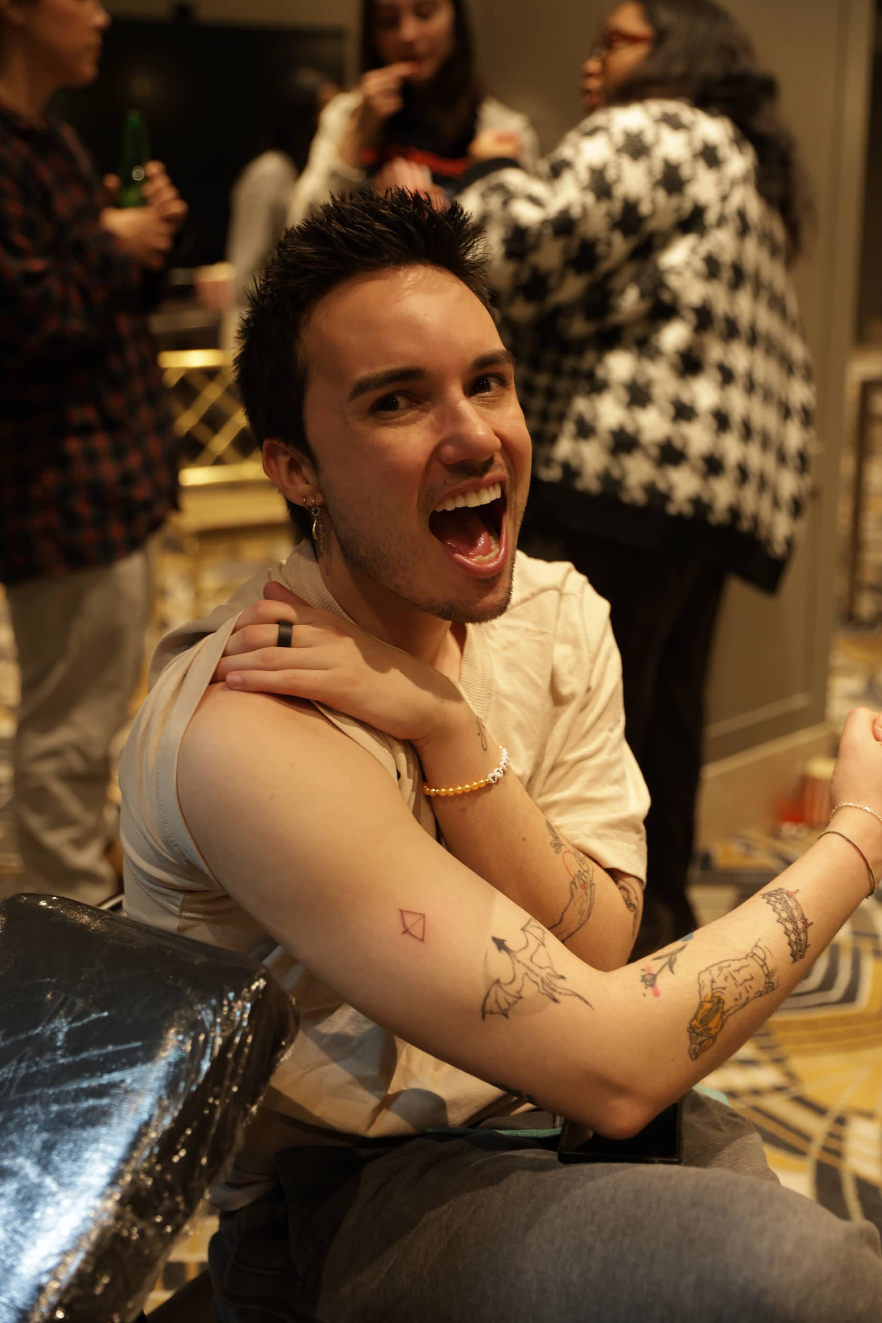 Smiling person showing fresh geometric and dragon tattoos on their arm in a busy indoor setting.
