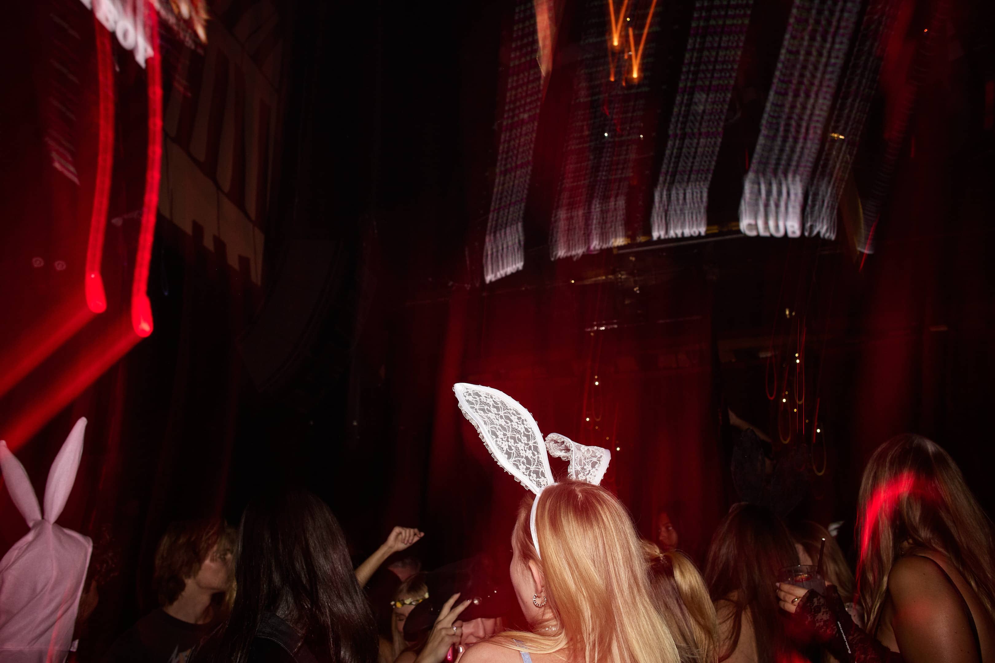 Crowd at a dark party, some wearing bunny ears headbands with red lighting effects.