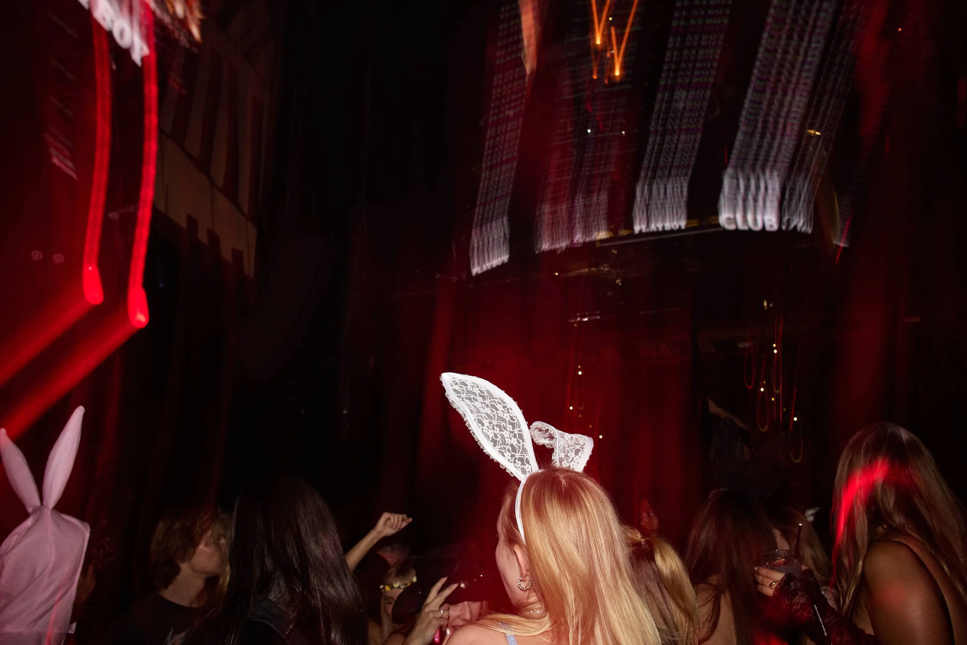 Crowd at a dark party, some wearing bunny ears headbands with red lighting effects.