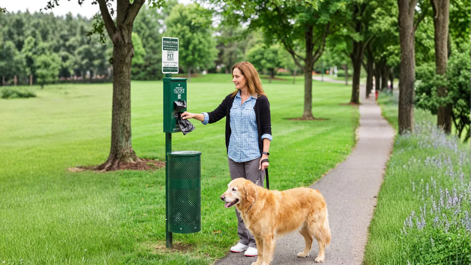 Woman and her golden retriever using a CoPS on Doody pet waste station along a community walking path