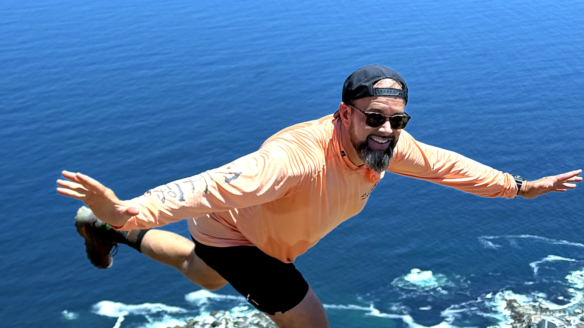 Chris Curry, arms outstretched on a clifftop high above the ocean