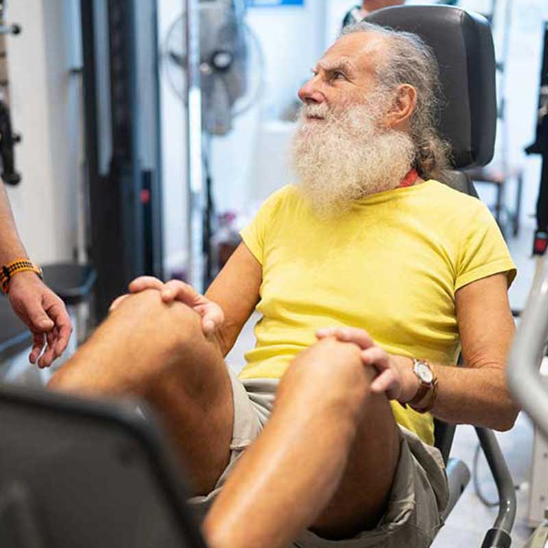 Older man doing supervised leg exercises in a physiotherapy gym setting