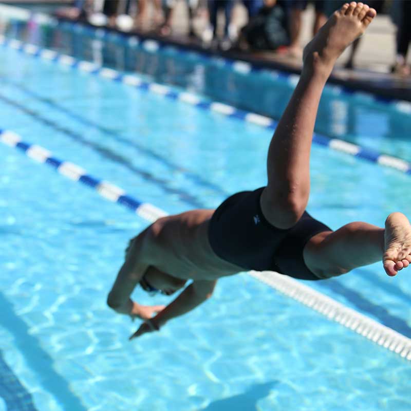Young boy diving from start block into outdoor swimming pool