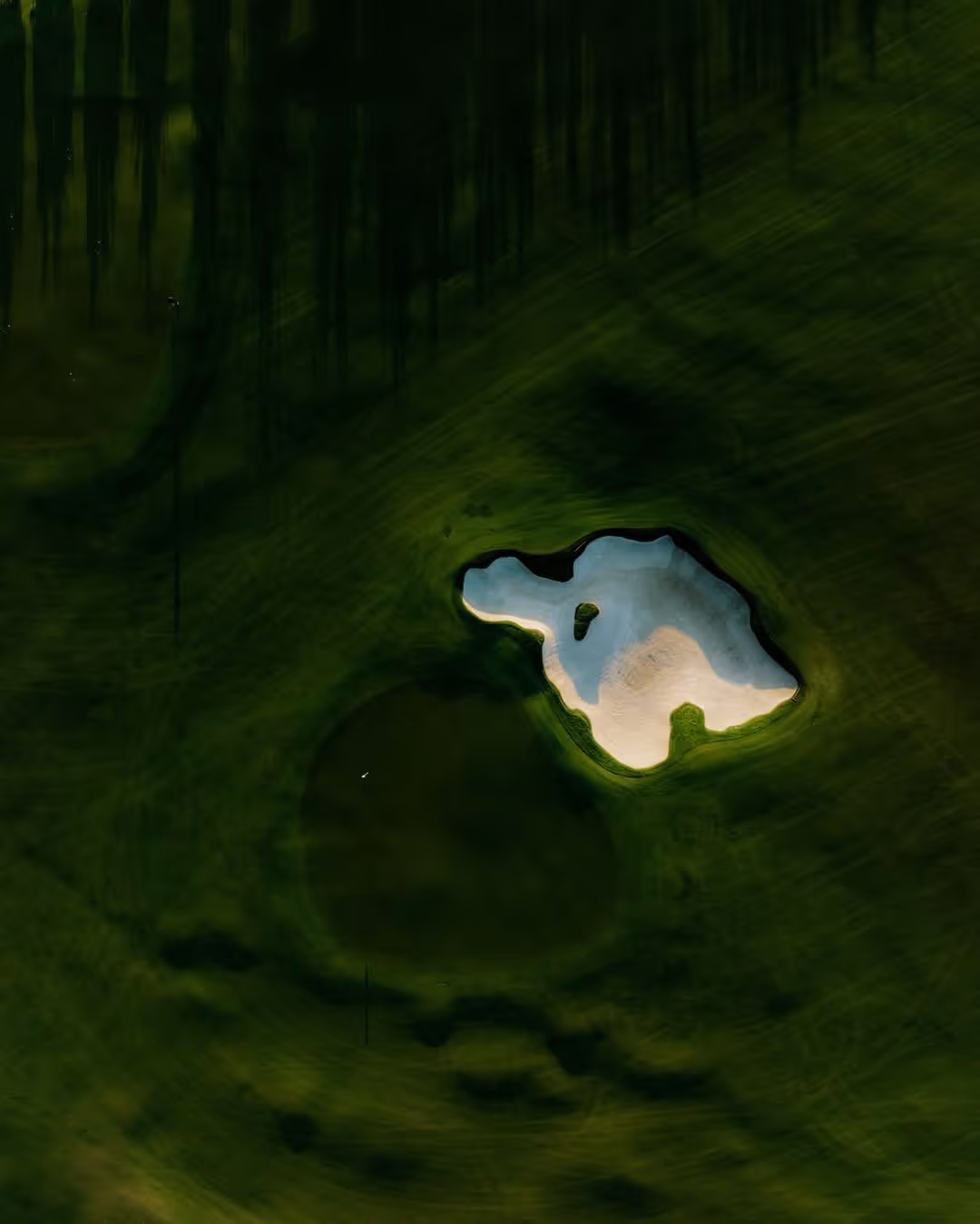 Aerial view of a golf course sand bunker surrounded by green grass.