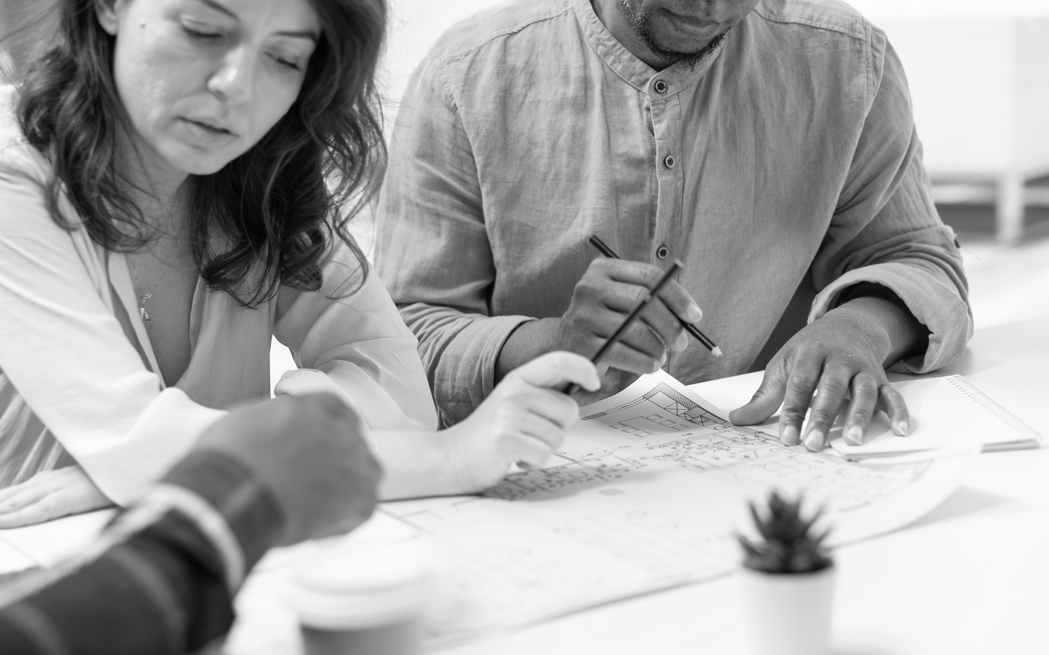 Deux personnes discutent et pointent un plan posé sur une table avec des crayons.
