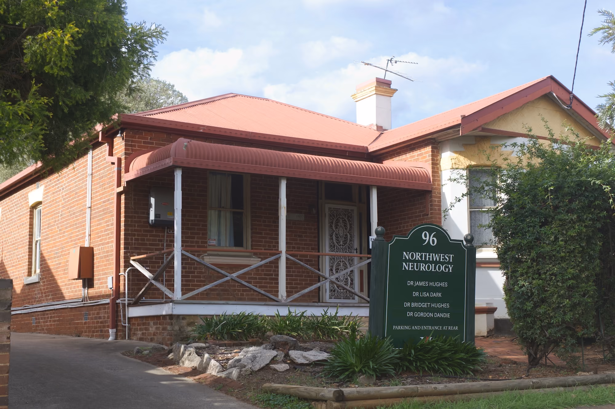 Brick building with red roof and porch, sign reading Northwest Neurology with doctors' names and address 96.