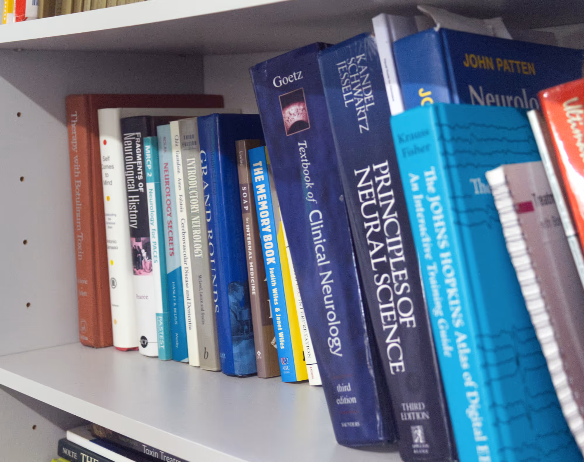 Bookshelf with neurology and medical textbooks including Principles of Neural Science and Clinical Neurology.